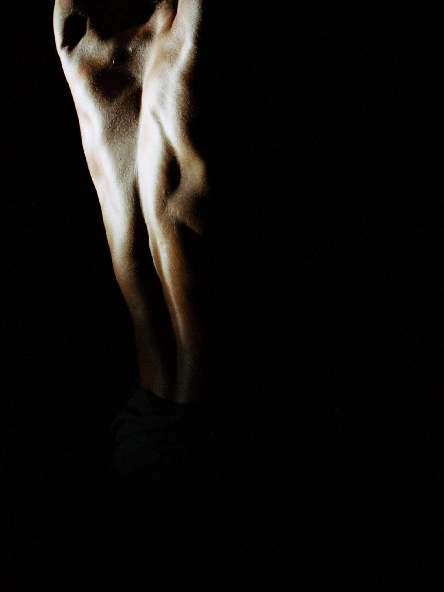 Una persona in piedi che ruota il busto, luce laterale che scolpisce la schiena.